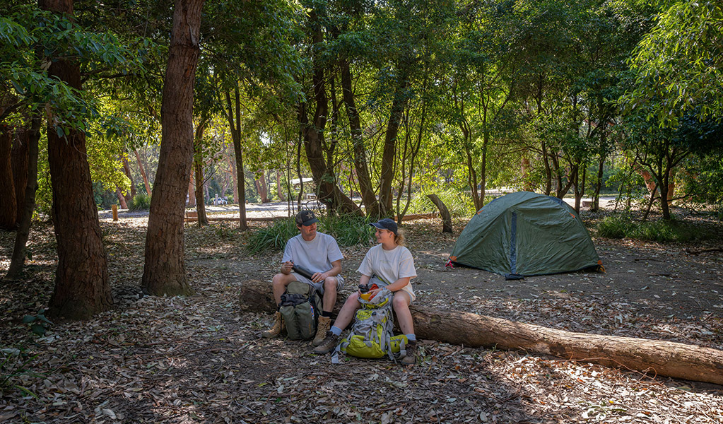 Campers resting on a log at Pretty Beach campground. Credit: John Spencer &copy; DCCEEW
