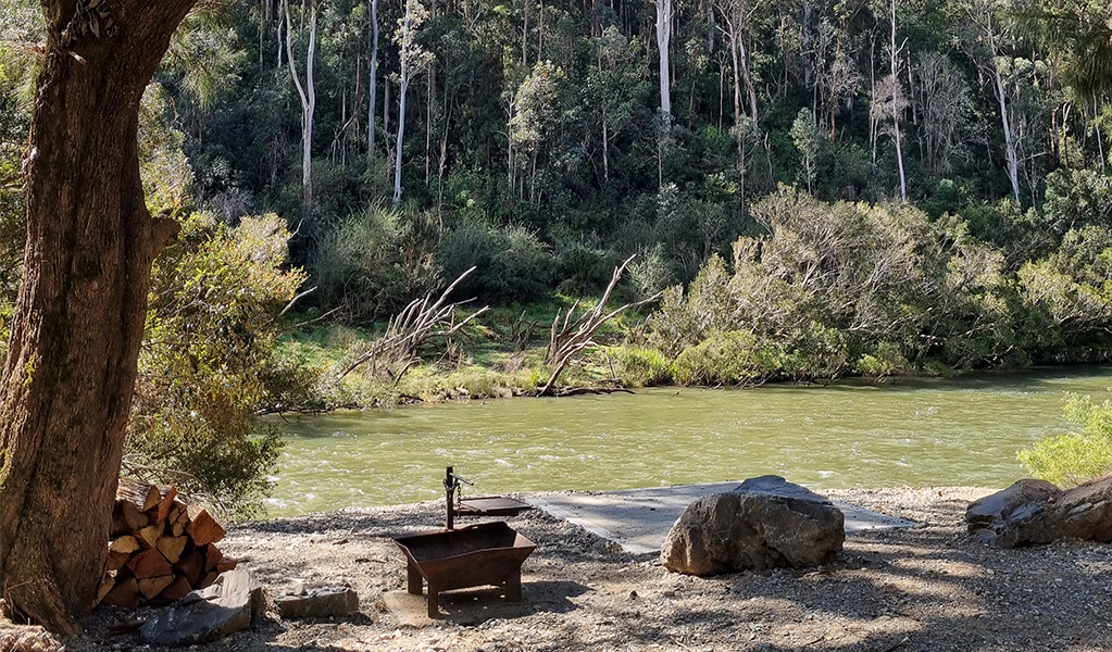 A campsite with a wood barbecue near the shore of the Nymboida River at Cod Hole campground and picnic area, Nymboi-Binderay National Park. Credit: Kit King &copy; DCCEEW