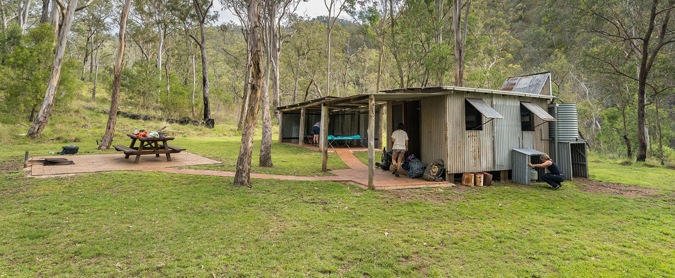 Multi-day hikers getting ready for an overnight stay at rustic Colwells Hut surrounded by bush in Oxley Wild Rivers National Park. &copy; DCCEEW