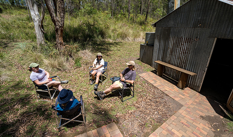 Four hikers relax on camping chairs outside a hut on The Green Gully Track. Credit: David Waugh &copy; DCCEEW