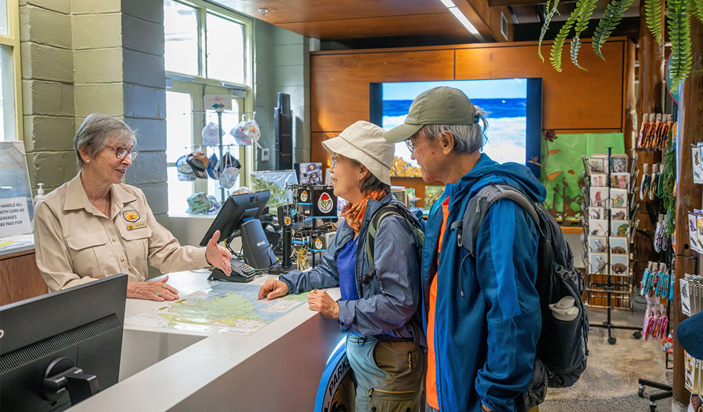 An NPWS staff member assisting 2 visitors inside the Royal National Park visitor centre at The Royal National Park. Credit: John Spencer &copy; DCCEEW