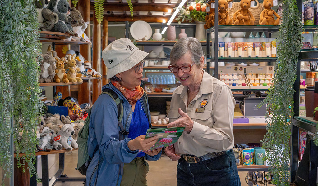An NPWS staff member helping a visitor inside the Royal National Park Visitor Centre shop. Credit: John Spencer &copy; DCCEEW