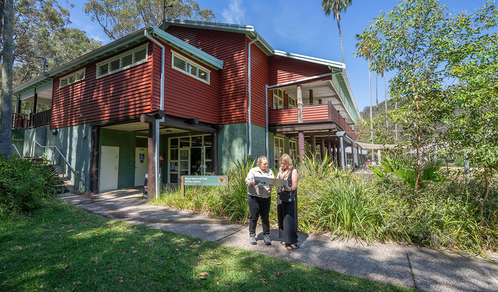 An NPWS staff member helping a visitor with a map outside the Royal National Park Visitor Centre. Credit: John Spencer &copy; DCCEEW