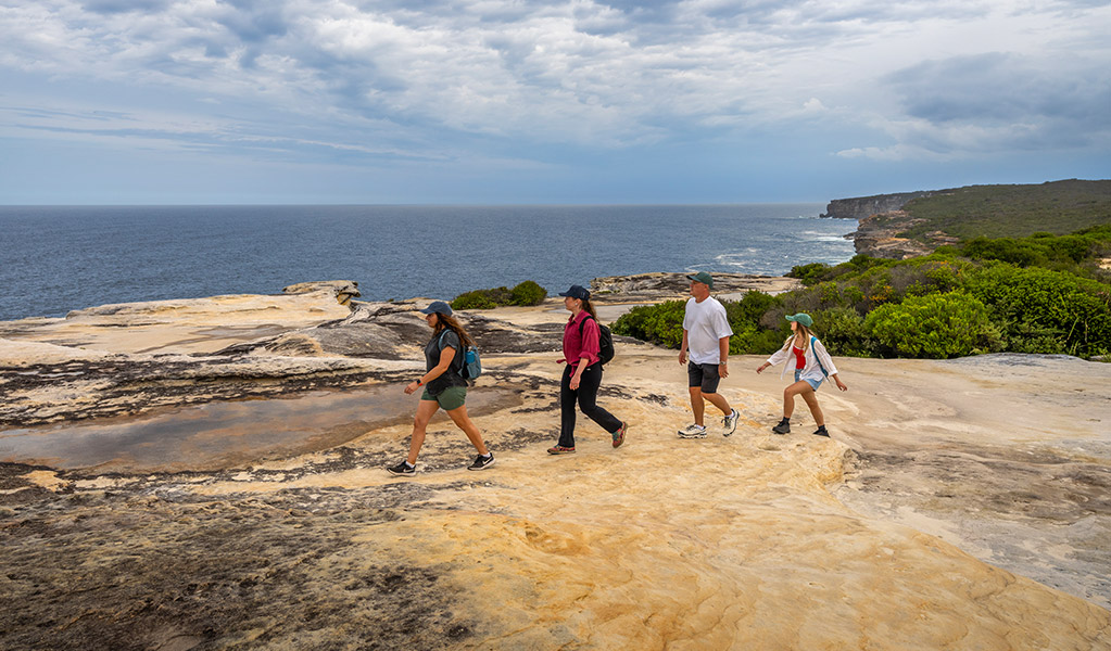 A family bushwalking on The Coast track near Bundeena, with cliffs and ocean in the distance. Credit: John Spencer &copy; DCCEEW