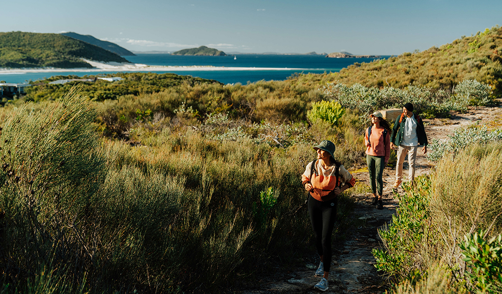  Three hikers on Tomaree Coastal Walk surrounded by coastal heathland, oceans views and islands in the background. Credit: Remy Brand &copy; Remy Brand
