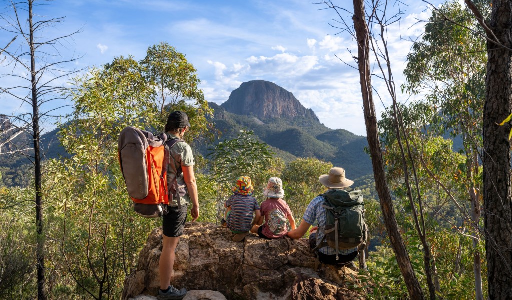 A family sitting on a rock looking out towards the peaks and spires of the Warrumbungles on Fans Horizon walking track in Warrumbungle National Park. Photo: john Spencer &copy; DCCEEW