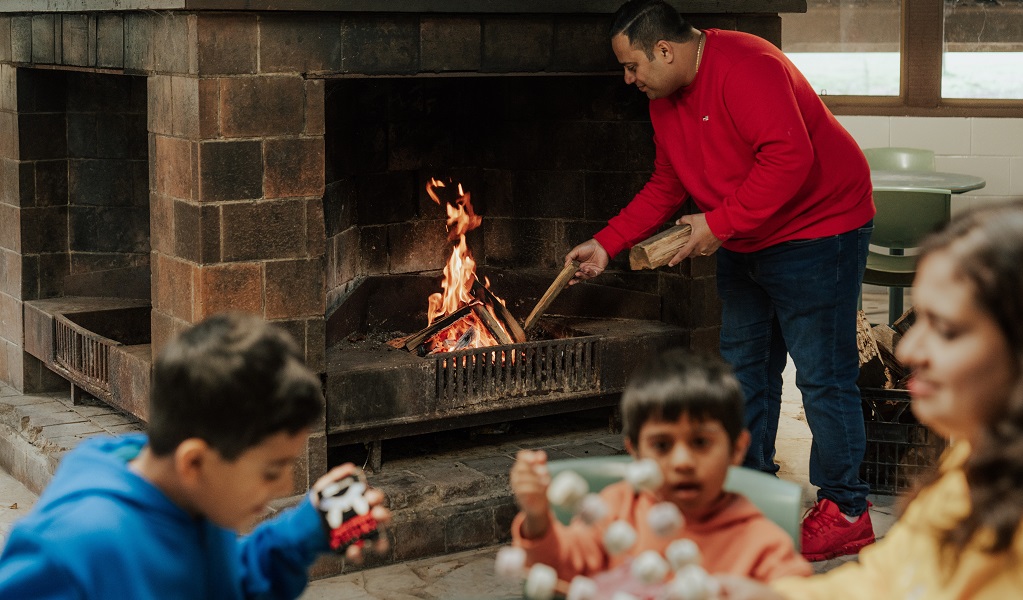 A man builds an open fire while his family prepare marshmallows for roasting, Barmah communal dining room. Credit: Remy Brand/DPE &copy; Remy Brand